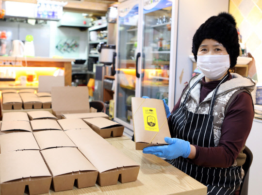 SK가 한마음한몸 운동본부의 노숙인을 위한 무료급식소인 명동밥집, 회현동 골목상점 연합체인 남촌상인회 등과 '소상공인 온기 배달 프로젝트'를 1월부터 시작한다. 윤남순 남촌상인회 회장이 명동밥집에 보낼 도시락을 포장하고 있다. <SK 제공>